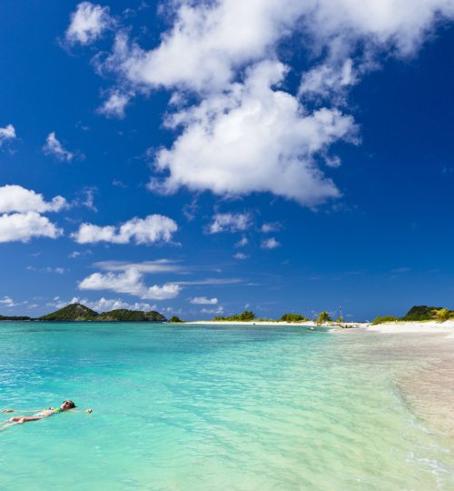 Woman floating on the turquoise waters of Sandy Island, a beautiful island just off Carriacou famous for its beauty, the white sandy beaches, clear waters and stunning coral reefs. It is a favorite anchorage for yachts, but it is also easily reached from Carriacou with a water taxi. Grenada, W.I. Canon EOS 5D Mark II